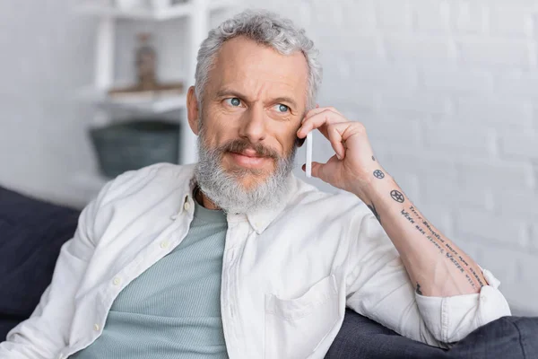 Hombre tatuado y barbudo con pelo gris hablando por teléfono móvil - foto de stock