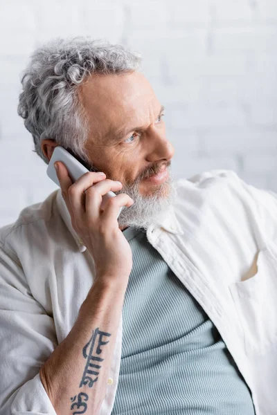 Hombre tatuado y barbudo con pelo gris hablando por celular - foto de stock