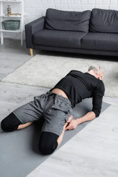 Hombre barbudo en ropa deportiva que se extiende en la alfombra de fitness en la sala de estar - foto de stock