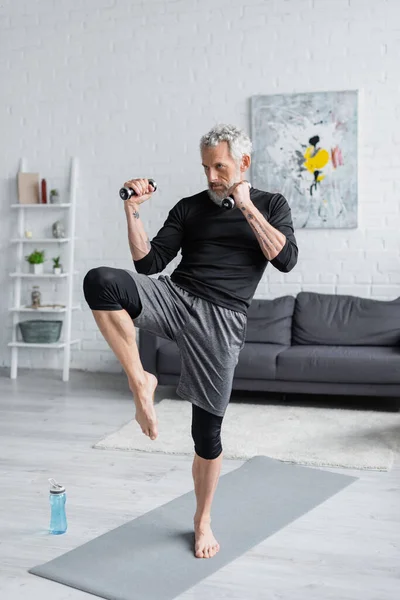 Volle Länge des starken und bärtigen Mannes, der im Wohnzimmer mit Kurzhanteln trainiert — Stockfoto