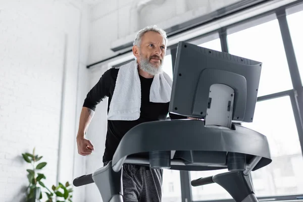 Bearded man with towel running on treadmill at home — Stock Photo