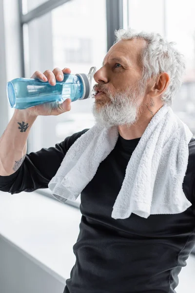 Barbudo hombre con pelo gris beber agua de deportes botella - foto de stock