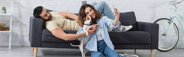 Felice giovane donna prendendo selfie con jack russell terrier e fidanzato musulmano, banner — Foto stock