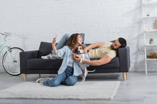 Sorridente giovane donna prendendo selfie con jack russell terrier e fidanzato musulmano — Foto stock