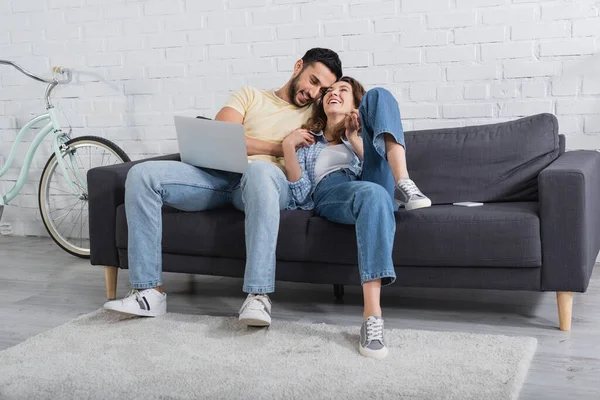 Feliz interracial freelancers sentado en el sofá con el ordenador portátil - foto de stock