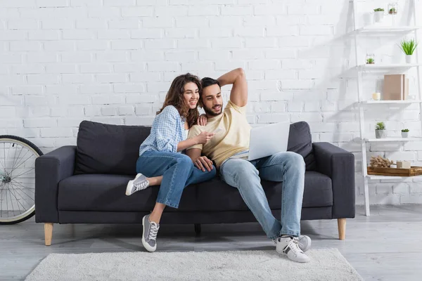 Happy woman pointing at laptop near muslim boyfriend — Stock Photo