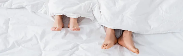 Top view of barefoot couple under blanket lying on bed, banner — Stock Photo