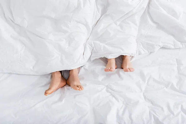 Top view of barefoot couple under blanket lying on bed — Stock Photo