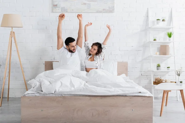 Acordado interracial casal olhando para o outro enquanto esticando na cama — Fotografia de Stock