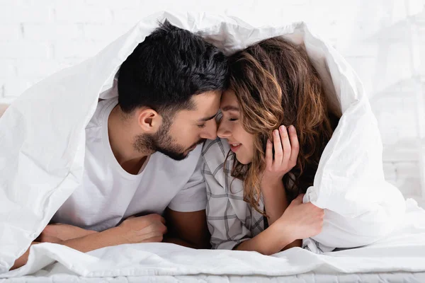 Feliz pareja interracial con los ojos cerrados acostado debajo de la manta - foto de stock