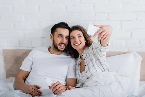 Feliz mujer tomando selfie con barbudo musulmán hombre en la cama - foto de stock