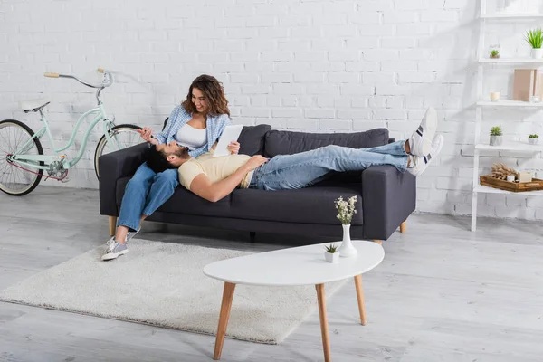 Musulmán hombre descansando en el sofá con la tableta digital cerca de novia feliz - foto de stock