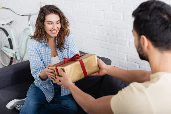 Homme musulman flou donnant cadeau enveloppé à petite amie heureuse dans le salon — Photo de stock