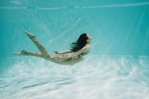 Zierliche junge Frau im weißen Badeanzug taucht in Swimmingpool — Stockfoto