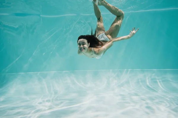 Happy young woman in white swimsuit diving in pool — Stock Photo