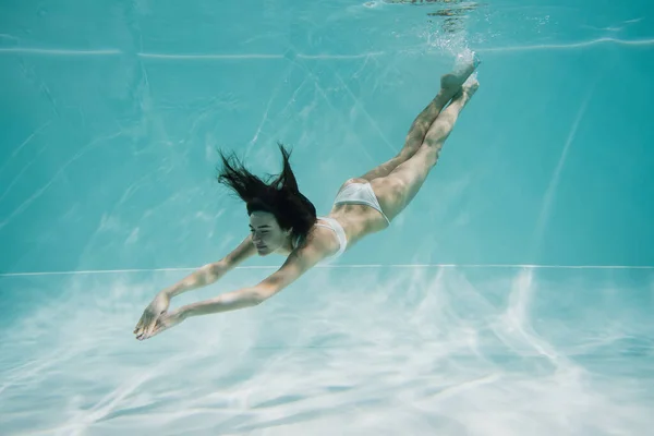 Anmutige junge Frau im weißen Badeanzug taucht in Pool — Stockfoto