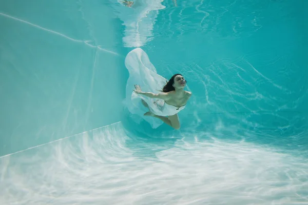 Pretty young woman in dress swimming in pool with blue water — Stock Photo