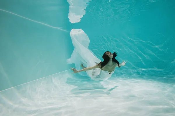 Pretty woman in dress diving in pool with blue water — Stock Photo