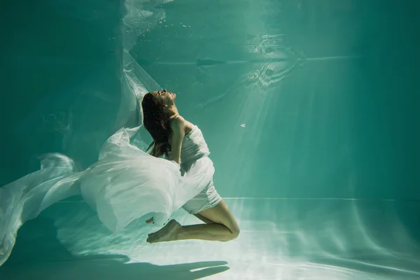 Side view of brunette young woman in dress swimming in pool with blue water — Stock Photo