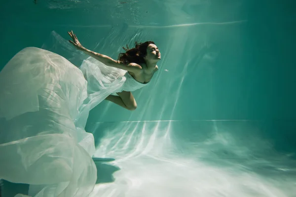 Brünette junge Frau im Kleid schwimmt in Pool mit blauem Wasser — Stockfoto