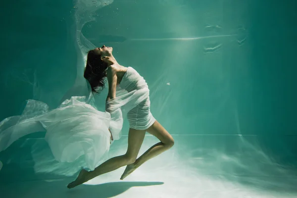 Mujer joven en vestido nadando en la piscina con agua azul - foto de stock