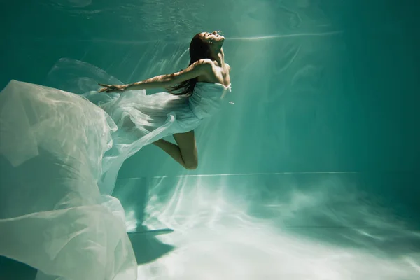 Brunette young woman in dress diving in pool — Stock Photo