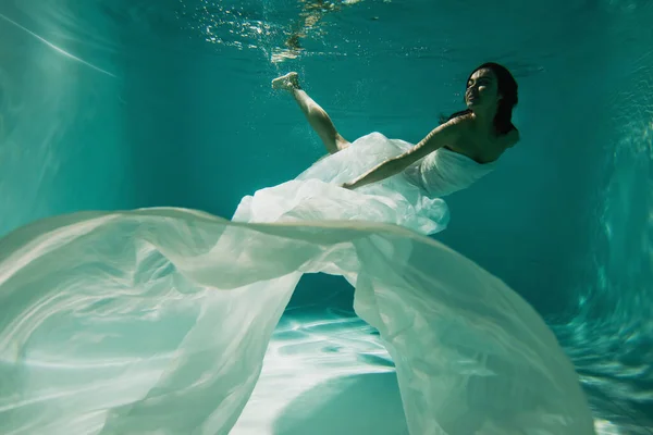 Молодая женщина в белом элегантном платье плавает в бассейне — стоковое фото