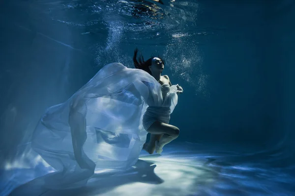 Iluminação na pacífica jovem mulher em branco elegante vestido de mergulho na piscina — Fotografia de Stock