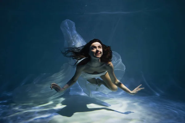 Lighting on happy young woman in white elegant dress swimming in pool — Stock Photo