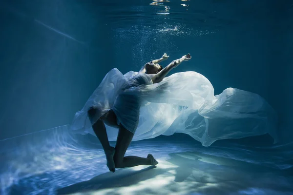 Iluminación en mujer descalza en vestido blanco nadando en la piscina - foto de stock