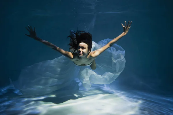 Iluminación en la joven sonriente en vestido elegante blanco nadar en la piscina — Stock Photo