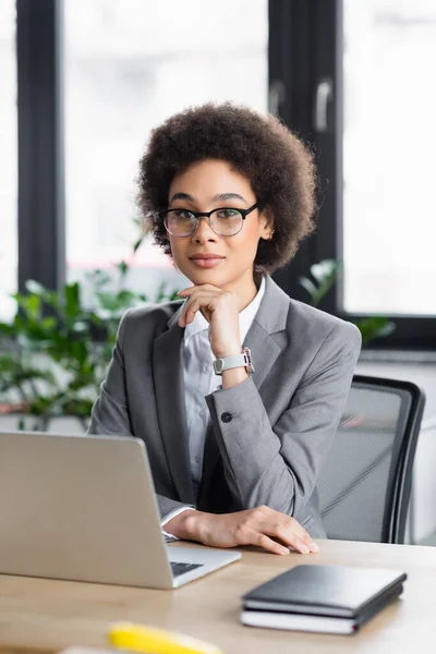 African american businesswoman sitting near blurred laptop and notebooks — Stock Photo