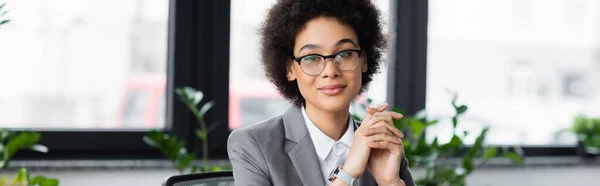 Lächelnde afrikanisch-amerikanische Geschäftsfrau, die im Büro in die Kamera schaut, Banner — Stockfoto