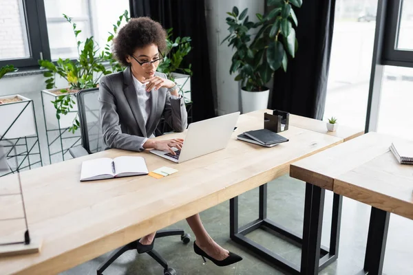 Empresaria afroamericana usando laptop cerca de cuadernos y notas adhesivas - foto de stock