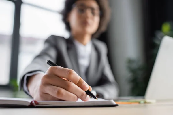 Afroamerikanische Geschäftsfrau auf verschwommenem Hintergrund schreibt auf Notizbuch — Stockfoto