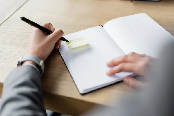 Cropped view of blurred businesswoman holding pen near sticky note on notebook — Stock Photo