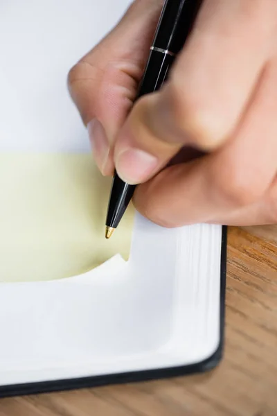 Close up view of businesswoman holding pen near sticky note on notebook — Stock Photo