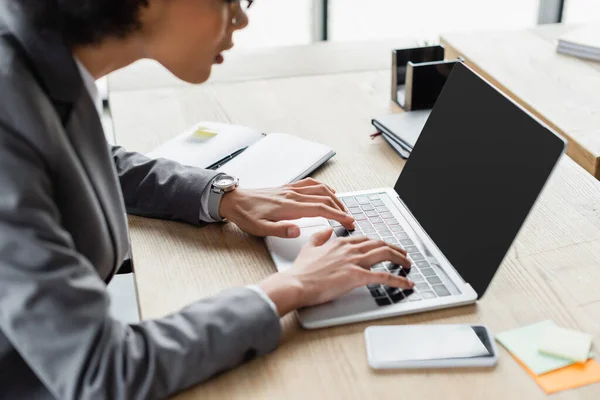 Cropped view of african american manager using laptop near cellphone on blurred foreground — Stock Photo