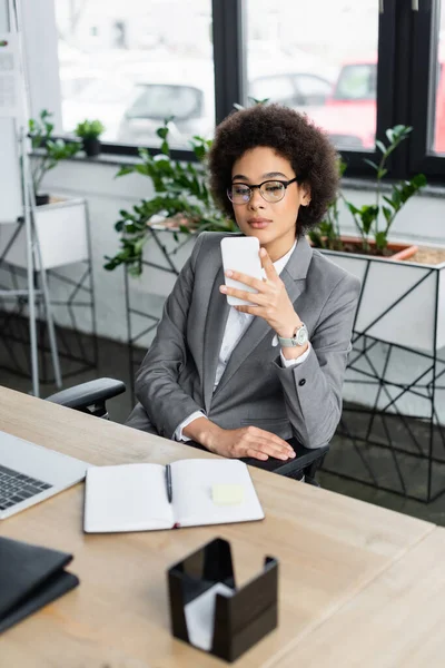 African american businesswoman using cellphone near blurred notebook and laptop — Stock Photo