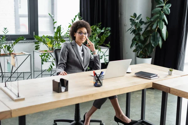 Gerente americano africano alegre falando no smartphone perto da mesa de trabalho — Fotografia de Stock