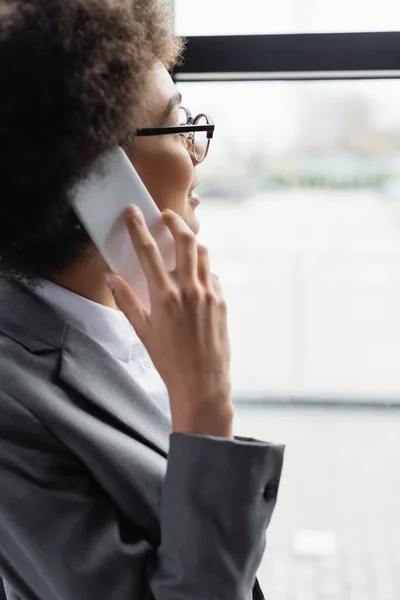 Smiling african american businesswoman in eyeglasses talking on smartphone — Stock Photo