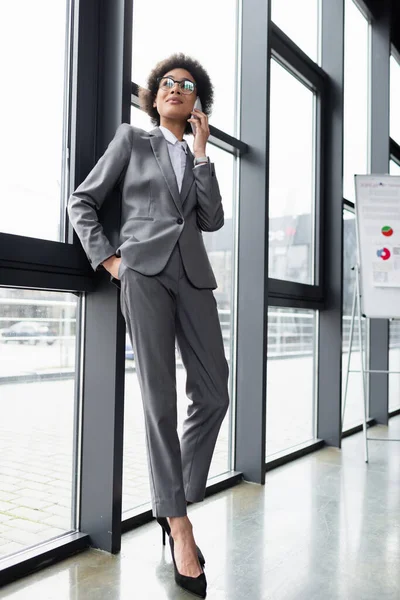 Afroamerikanische Geschäftsfrau telefoniert am Fenster mit Handy und verschwommenem Flipchart — Stockfoto