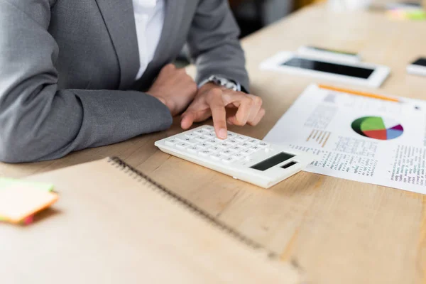 Vista recortada de la mujer de negocios utilizando la calculadora cerca de documento y cuaderno borroso - foto de stock