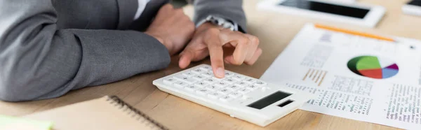 Zugeschnittene Ansicht des Managers mit Taschenrechner in Papiernähe mit Diagrammen auf verschwommenem Hintergrund, Banner — Stockfoto