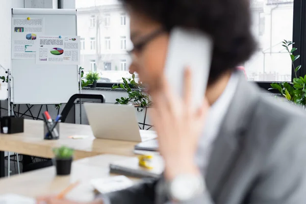 Graphs on flipchart near blurred african american businesswoman talking on cellphone — Stock Photo