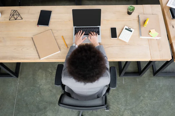Overhead view of african american businesswoman using laptop near smartphone and calculator — Stock Photo