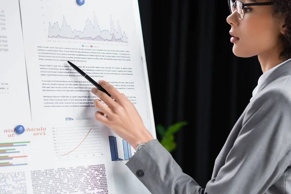 Side view of african american manager in eyeglasses pointing at document on flipchart — Stock Photo