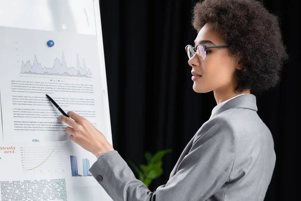 Vue latérale de la jeune femme d'affaires afro-américaine avec stylo pointant vers le papier sur tableau à feuilles mobiles — Photo de stock