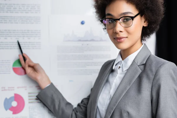 Afrikanischer Manager blickt in Kamera in der Nähe von verschwommenem Flipchart — Stockfoto