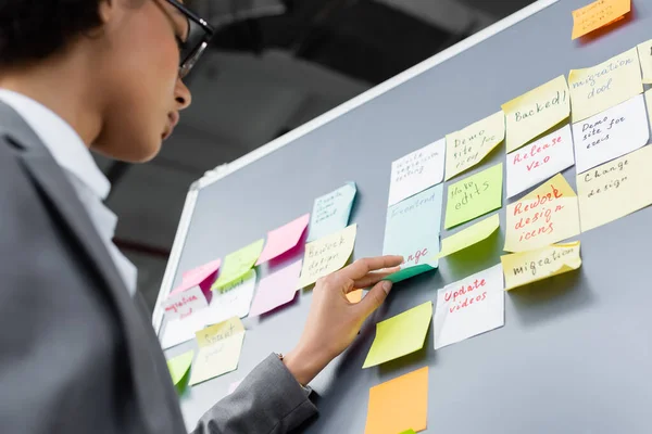 Low angle view of african american manager standing near board with sticky notes — Stock Photo